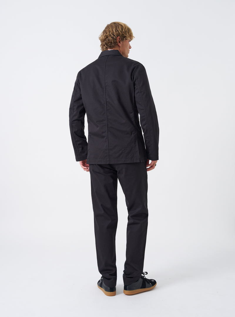 Side angled view of a male model wearing the Black Twill London Jacket in a studio setting with a clean neutral background, displaying the silhouette, sleeve length, and jacket drape when worn.