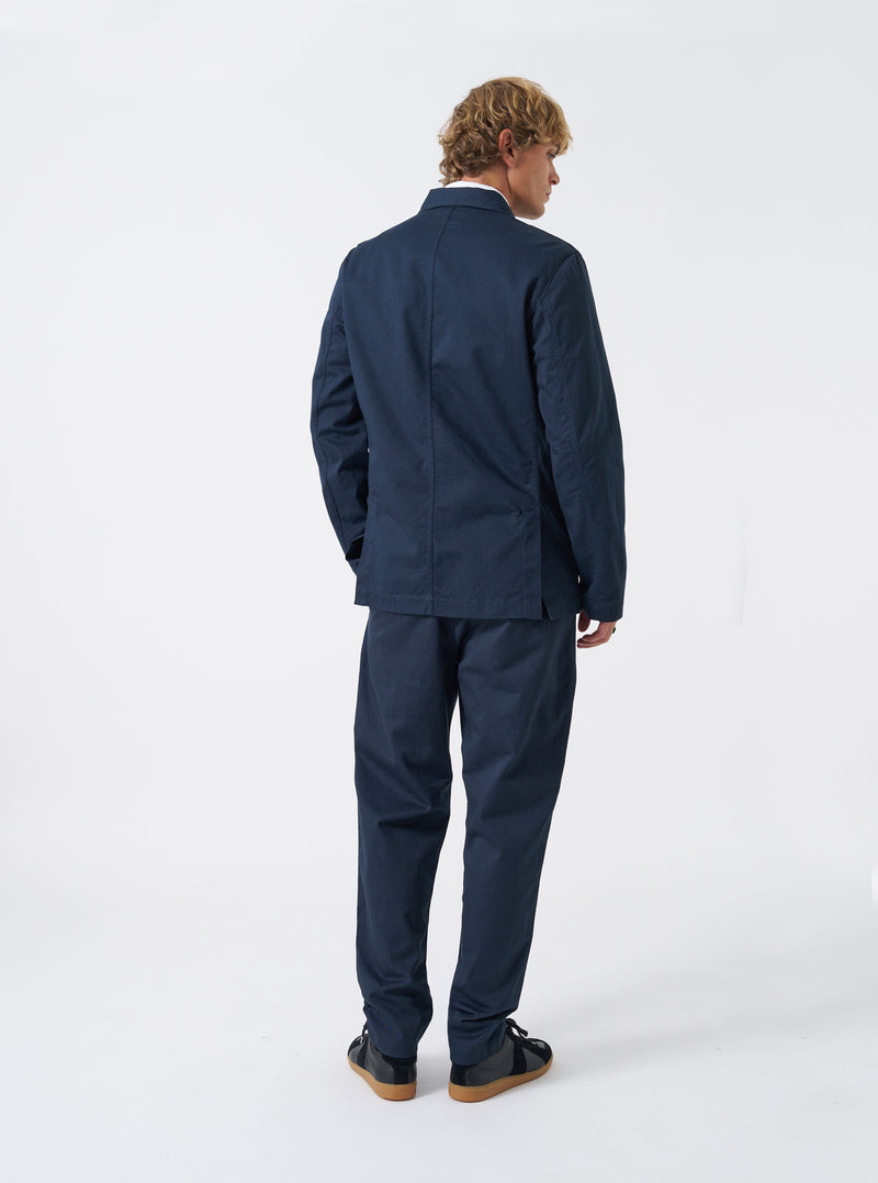 Three-quarter view of a male model wearing the Navy Twill London Jacket in a bright studio environment, demonstrating the jacket drape, arm length, and deep navy blue color against a plain backdrop.