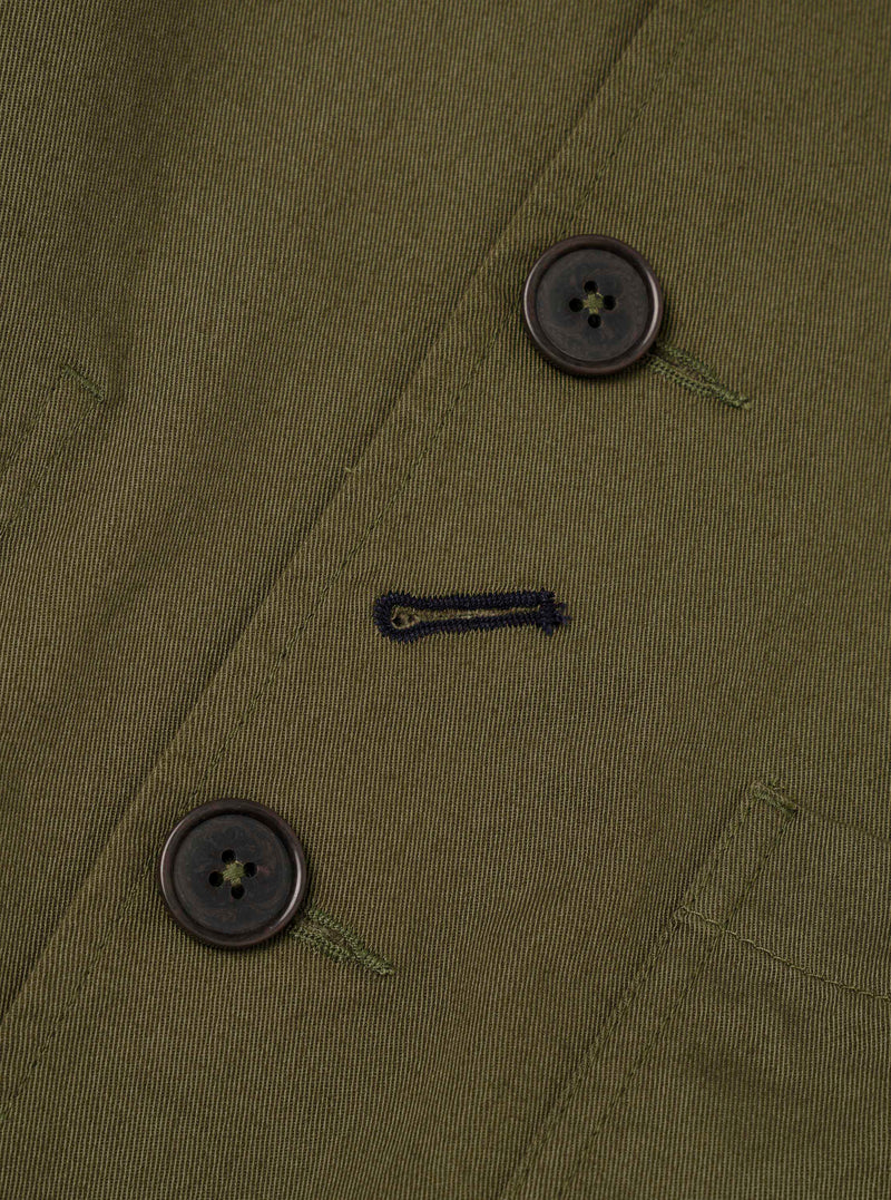 Close-up detail shot of the Light Olive Twill Bakers Chore Jacket against a plain backdrop, displaying the light olive twill weave pattern, durable button stitching, angled pocket edge, and fabric finish.