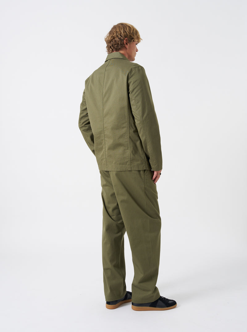 Angled side view of a model wearing the Light Olive Twill Bakers Chore Jacket in a bright studio setting. Shows the jacket fit along the sleeves, shoulder seams, and side profile in light olive green twill.