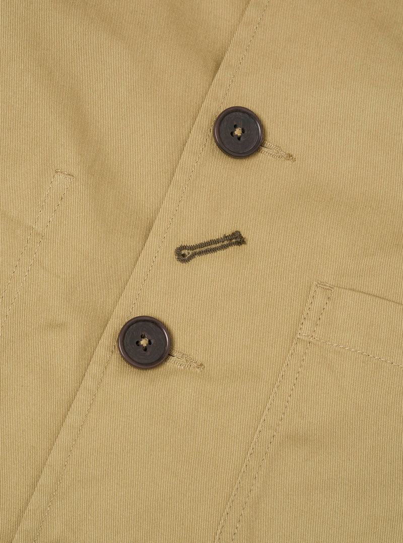 Close-up detail view of the Sand Twill Bakers Chore Jacket on a white background. Highlights the front placket buttons, distinctive diagonal buttonhole detail, and woven sand tan cotton twill texture.