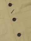 Close-up of the sand twill Bakers Jacket, showcasing the fabric texture, dark buttons, and pocket stitching. The jacket is laid flat on a neutral surface.