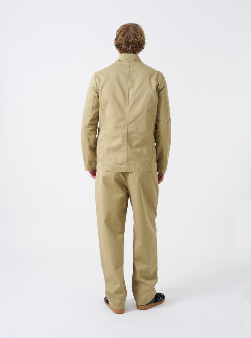 Rear view of a model wearing the Sand Twill Bakers Chore Jacket in a light studio background. The model stands facing away, displaying the drape, fit across the back, and overall silhouette.