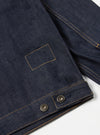 Close-up of the Indigo 13oz Selvedge Denim Trucker Jacket on a white surface. Shows the dark indigo denim, selvedge detailing, and metal buttons.