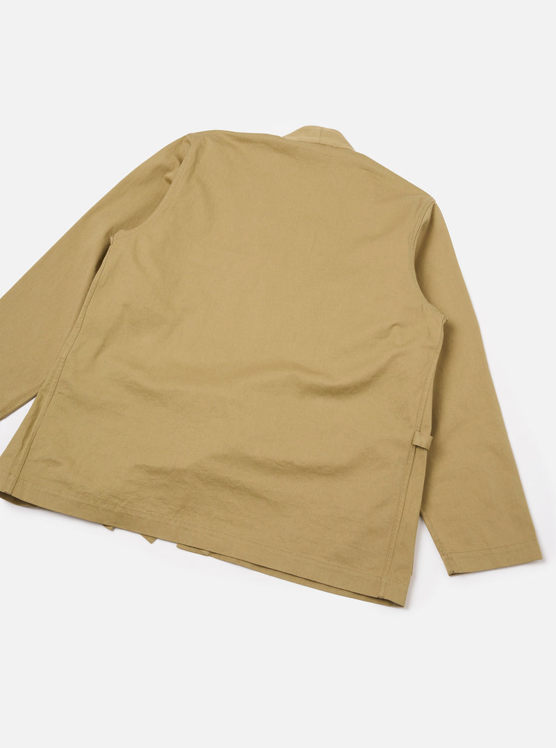 Rear view of the Sand Twill Kyoto Work Jacket isolated on a plain off-white backdrop. Shows the clean back seam construction, drop-shoulder sleeve design, and relaxed fit of the sand twill garment.