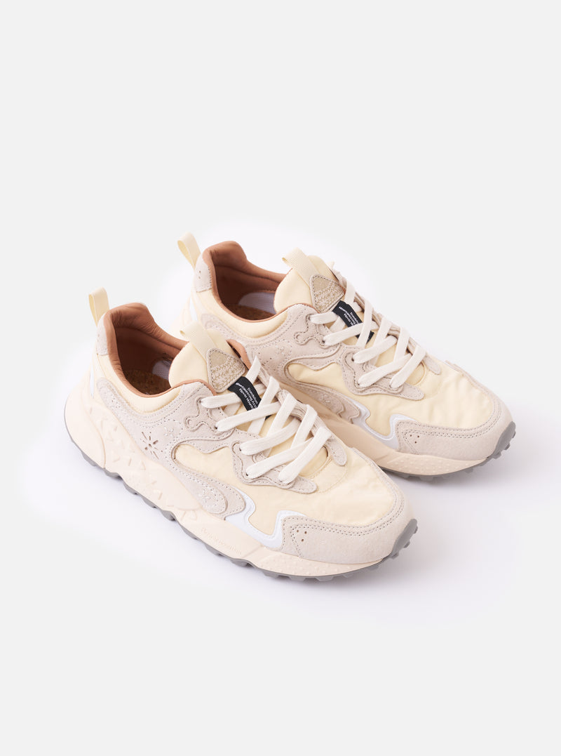 The Flower Mountain Milk/Light Beige Suede/Nylon Rulis Uni sneaker is shown in a detail view as a flat lay against a plain white background. The image highlights the layered construction of the footwear, featuring overlapping light beige suede panels and milky white technical fabric. The thick, moulded rubber sole with a textured sidewall and the webbing pull tab at the heel are prominent.