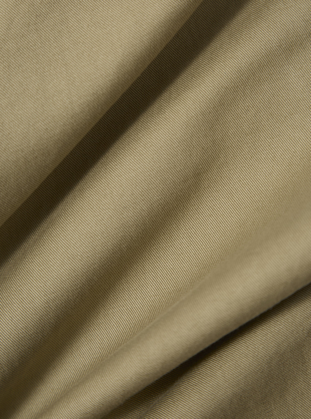 Close-up of the sand twill military chino fabric. The material is folded, showing the texture and color of the twill. The background is a plain surface.