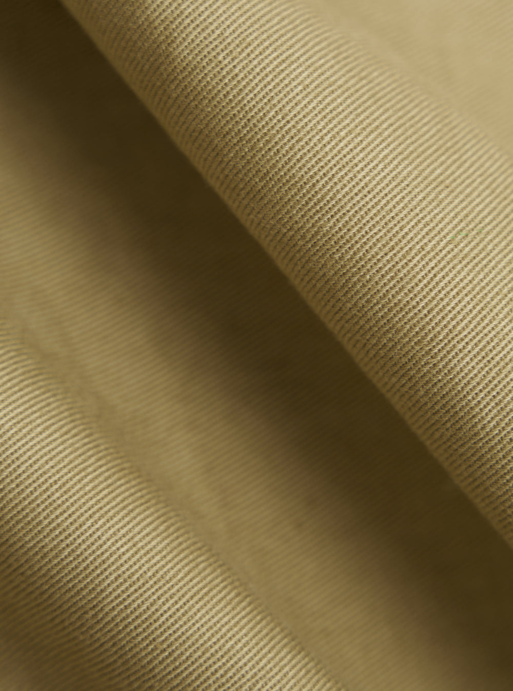 Close-up of the Sand Twill Curved Pant fabric. The material is a textured, sand-colored twill. The image is cropped to highlight the fabric's weave and texture.