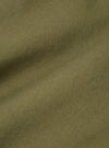 Close-up of the light olive twill fabric of a Baker's Jacket, showing the texture and color. The background is a plain surface.