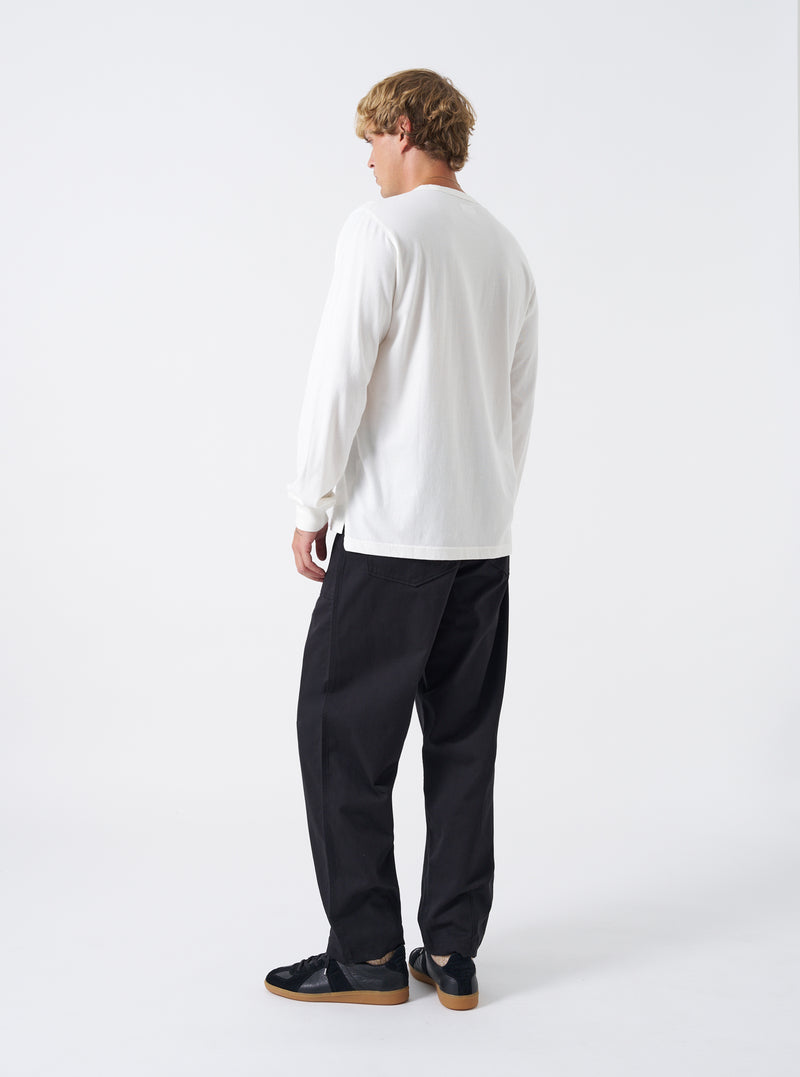 Rear view of a male model wearing the Black Twill Fatigue Pant set against a plain studio backdrop. Shows the fit across the seat, rear buttoned patch pockets, waist adjustment tabs, and straight-leg drop in black cotton twill.