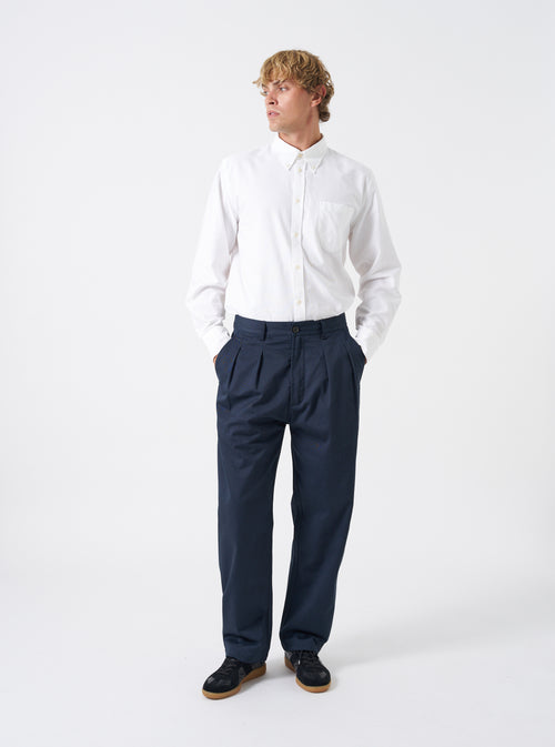 Front view of a model wearing the Navy Twill Double Pleat Pant on a plain backdrop. The trousers feature a roomy wide fit and double pleats, styled with smart footwear to show overall length and drape.
