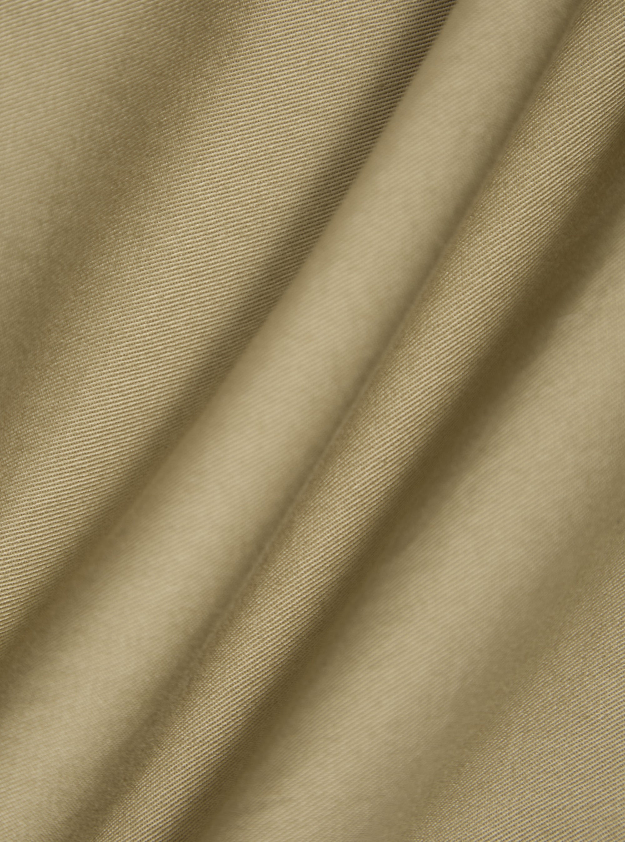 Close-up of the sand twill double pleat pant fabric. The material is draped to show texture. The background is a plain white surface.