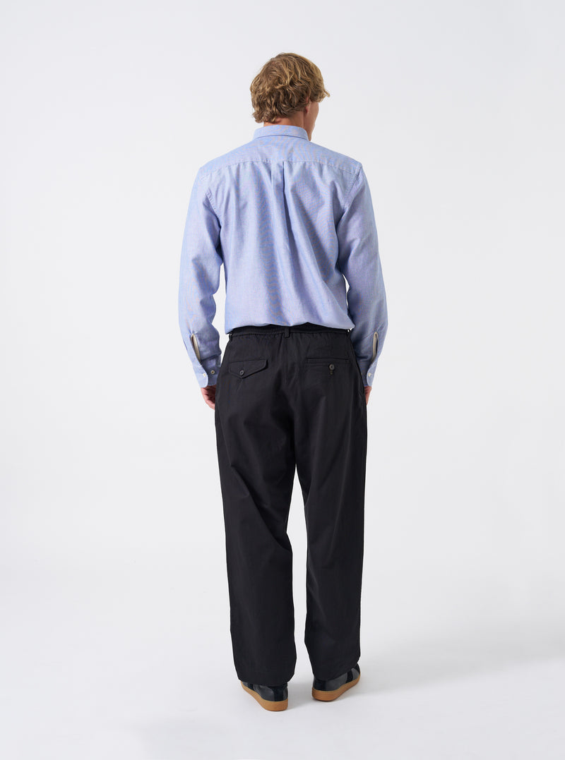 Additional shot of a model wearing the Black Twill Pleated Track Pant on a neutral background. Highlights the movement and drape of the pleated black twill fabric along with the casual tapered fit.