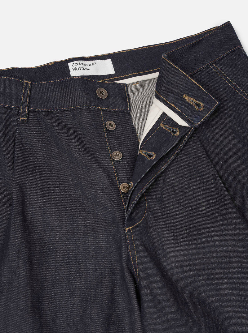 Detailed view of the Indigo 13oz Selvedge Denim Duke Pant - Longer Length worn by a model in a studio setting. Prominent features include the dark blue selvedge denim texture, precise pocket stitching, and front button closure details.