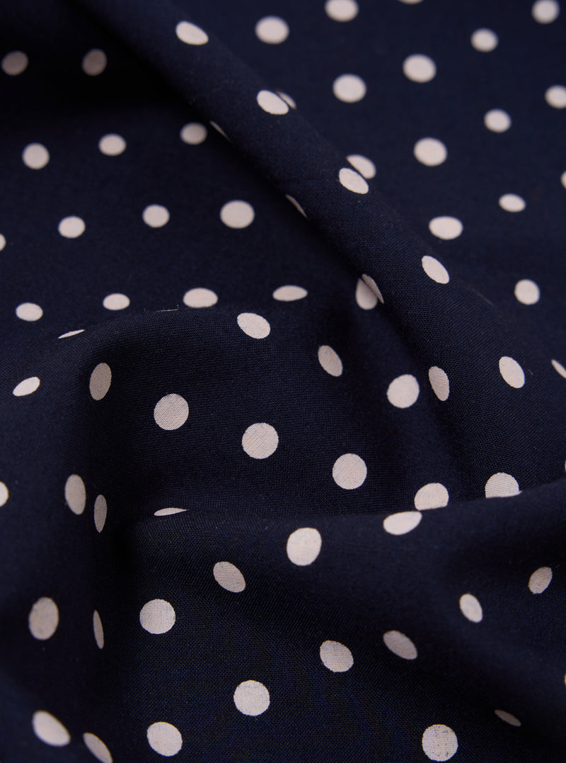 Close-up of a Navy Dot Print Short Scarf, showing the fabric's texture and pattern. The scarf is draped on a flat surface, highlighting the navy background and white polka dots.