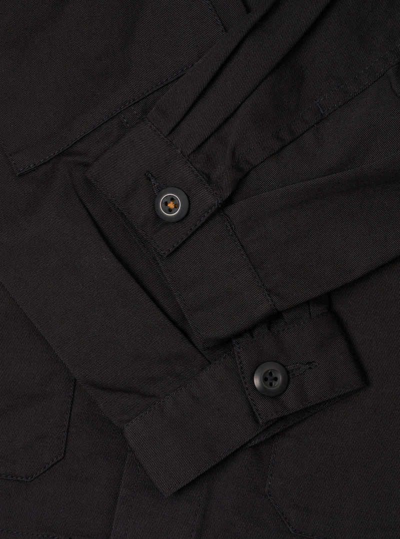 A close-up detail shot of the Black Twill MW Fatigue Jacket against a solid white background. The image highlights the internal drawstring waist adjustment, sturdy seam detailing, and concealed button front closure.
