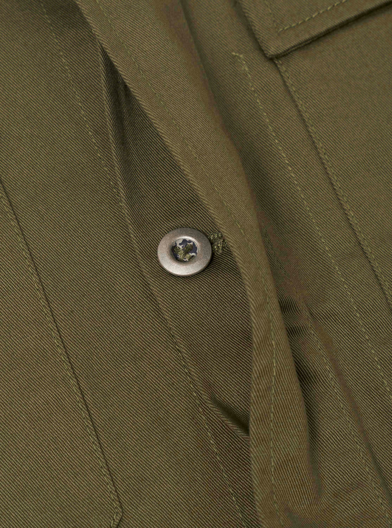 A close-up view of the Light Olive Twill MW Fatigue Jacket against a plain white backdrop. The photo highlights the chest flap pocket, neat collar stitching, and the distinct diagonal weave of the light olive cotton twill.