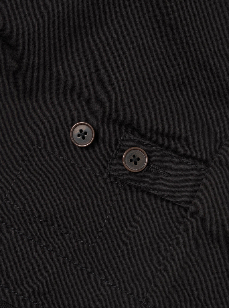 Close-up detail shot of the Black Twill Field Waistcoat against a plain white background. The focus is on the angled flap patch pocket construction, reinforced stitching, and sturdy waist adjustment buckle.