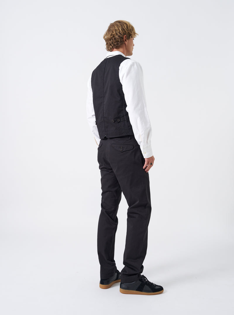 A model wearing the Black Twill Field Waistcoat is shown from the back against a clean studio background. The photograph highlights the adjustable rear buckle cinch, tailored back seams, and comfortable fit.