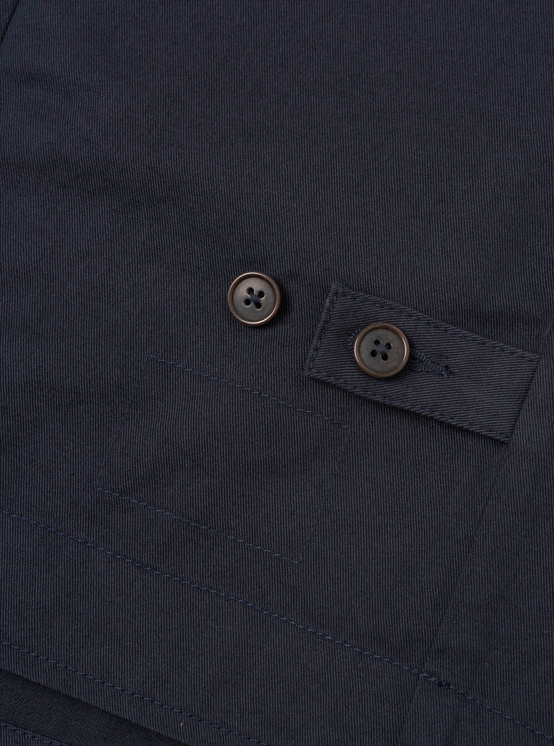 Angled close-up view of the Navy Twill Field Waistcoat presented against a plain white backdrop. The shot showcases the inner neck brand tag, durable navy twill fabric, tonal button closure detail, and clean inner pocket finishing stitching.