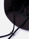 The cableami Black Baker Back Satin Cotton Metro Hat is shown from a rear three-quarter angle as a flat lay against a plain white background. The image highlights the six-panel construction of the crown and the circular brim, showcasing the smooth, matte finish of the black back-satin cotton fabric. A black adjustable and detachable drawcord with plastic clips is visible, attached to the sides of the hat.
