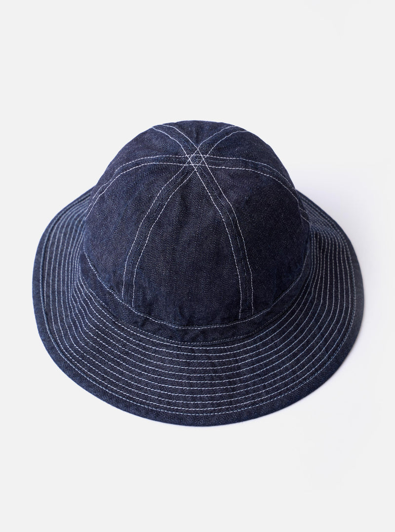 The cableami Indigo 10oz Denim Metro Hat is shown from a rear three-quarter angle as a flat lay against a plain white background. The image highlights the hat's rounded crown, downward-sloping brim with tonal stitching, and an adjustable strap cord featuring a plastic toggle.