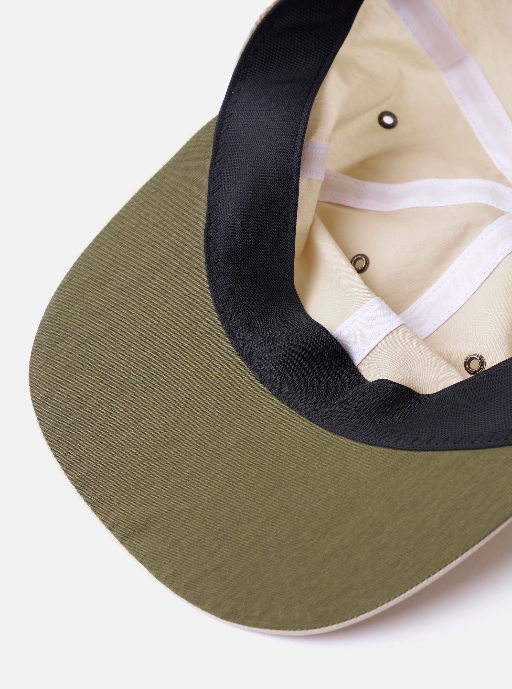 The cableami Ivory/Olive Cotton/Nylon B.B Cap is shown in a detail view from the back as a flat lay against a plain white background. The image highlights the adjustable olive green fabric strap with a metal buckle and the ventilation eyelets on the ivory crown.
