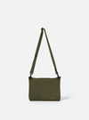 The master-piece x Universal Works Olive Canvas Sacoche is shown from a rear angle as a flat lay against a plain white background. The image highlights the back of the bag, featuring a small zippered pocket and the adjustable olive webbing strap. The durable olive green canvas fabric is the prominent feature.