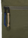 The master-piece x Universal Works Olive Canvas Sacoche is shown from a rear angle as a flat lay against a plain white background. The image highlights the back of the bag, featuring a clean olive green canvas surface and the attachment points for the thin, adjustable black crossbody strap.