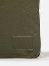 The master-piece x Universal Works Olive Canvas Sacoche is shown from a rear angle as a flat lay against a plain white background. The image highlights the back of the olive green bag, featuring a small woven brand label and the attachment points for the adjustable webbed shoulder strap.