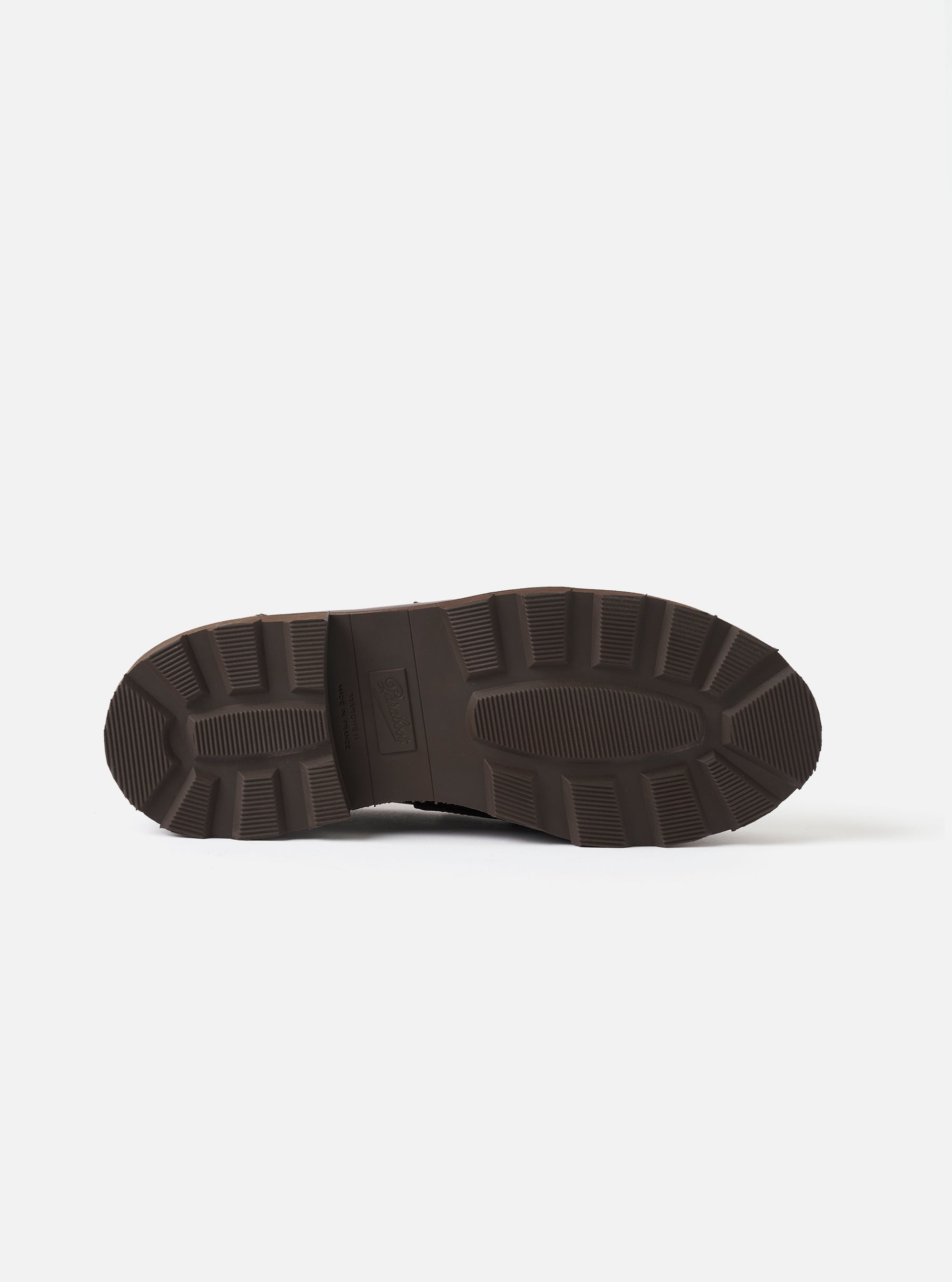 Underside of the Paraboot Reims Marche in cafe leather, showing the dark brown chunky rubber outsole. Deep directional lugs run around the heel and forefoot, with a ribbed central zone and embossed Paraboot branding on the shank. Shot on a plain light grey studio backdrop.