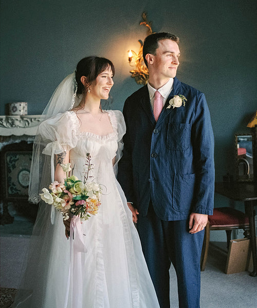 Couple in wedding attire standing in a room with a fireplace and decorative wall lights.
