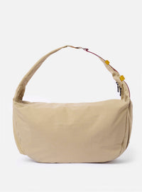The master-piece x Universal Works Beige Large Canvas Shoulder Bag is shown as a flat lay against a white background. The bag features a rectangular shape with two flat top handles, a front outer pocket with a press stud fastening, and a small dual-branded label. The beige canvas material has a durable, textured appearance.