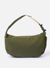 The master-piece x Universal Works Olive Large Canvas Shoulder Bag is shown as a flat lay against a white background. The large tote features two top handles, a front patch pocket with a velcro closure, and a visible collaborative logo patch. The fabric is a durable olive green canvas.