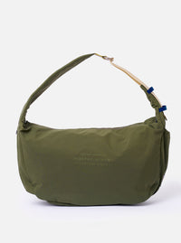 The master-piece x Universal Works Olive Large Canvas Shoulder Bag is shown as a flat lay against a white background. The large tote features two top handles, a front patch pocket with a velcro closure, and a visible collaborative logo patch. The fabric is a durable olive green canvas.