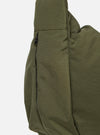 The master-piece x Universal Works Olive Large Canvas Shoulder Bag is shown from the back as a flat lay against a plain white background. The image highlights the bag's olive green canvas construction, featuring a rear compartment with a hook and loop fastener and a webbing strap for attaching to a suitcase handle.