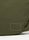 The master-piece x Universal Works Olive Medium Canvas Shoulder Bag is shown from the back as a flat lay against a plain white background. The image highlights the horizontal webbing strap designed for a suitcase handle and the adjustable, detachable shoulder strap. The bag is made from olive green canvas and features a clean, rectangular silhouette.