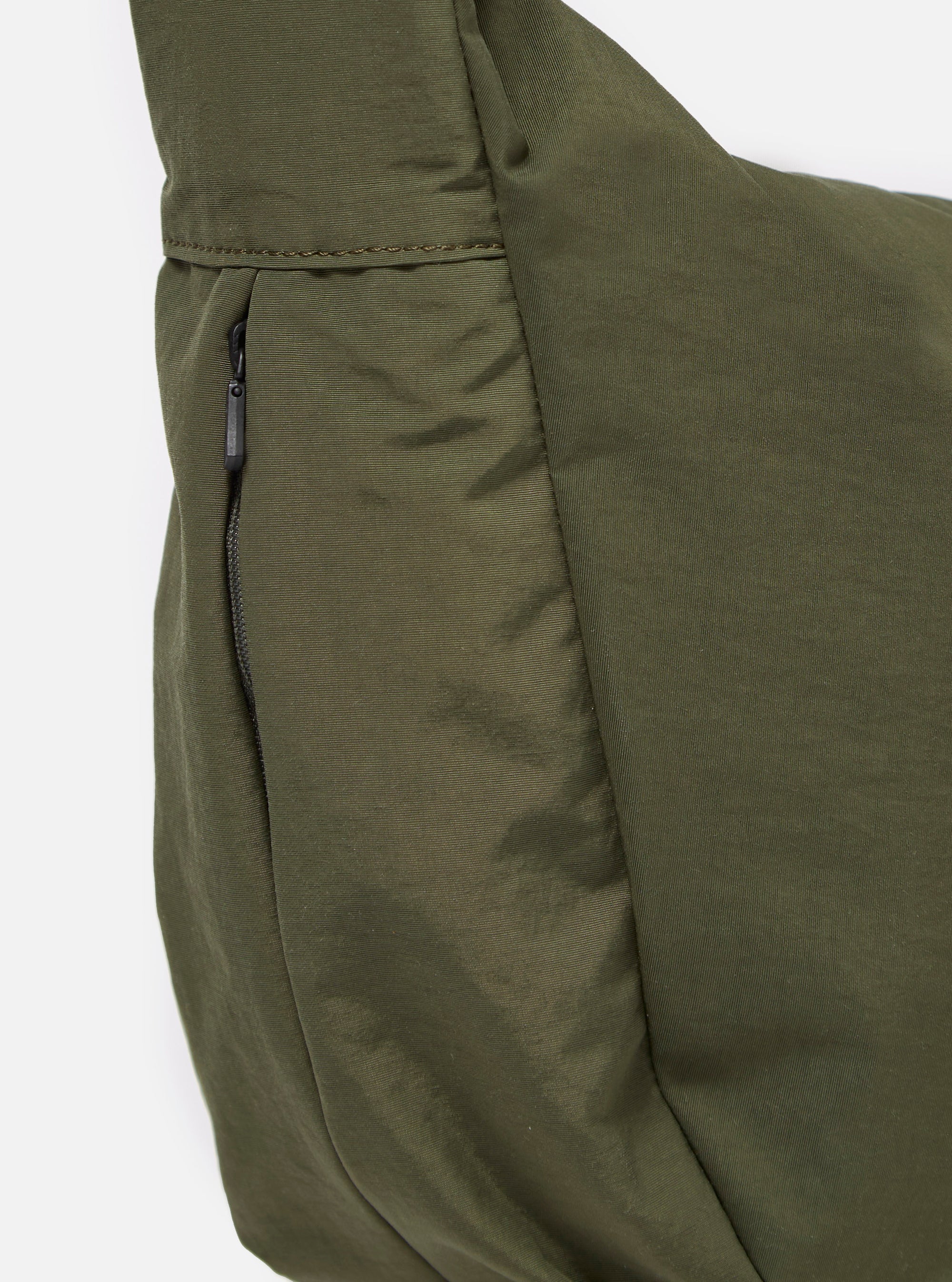The master-piece x Universal Works Olive Medium Canvas Shoulder Bag is shown from the back as a flat lay against a white background. The image highlights the adjustable olive webbing strap, the rear compartment, and the smooth canvas fabric.