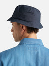 A model wears the Navy Recycled Polytech Beach Hat, shown from a rear three-quarter angle against a plain, neutral background. The bucket-style hat features a wide, downward-sloping brim with tonal parallel stitching and a structured crown. The navy blue fabric has a smooth, technical finish.