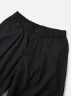 Close-up of the Charcoal Tropical Suiting Oxford Pant on a white surface. The charcoal pants have an elastic waistband and a button closure.