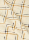 Close-up of the Ecru PJ Plaid Boxer Short fabric. The material is ecru with a plaid pattern in brown and black. The fabric is folded on a white surface.