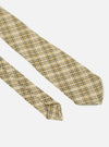 Close-up of the Sand Picnic Plaid Tie on a white surface. The tie features a tan, white, and brown plaid pattern. The fabric has a textured appearance.