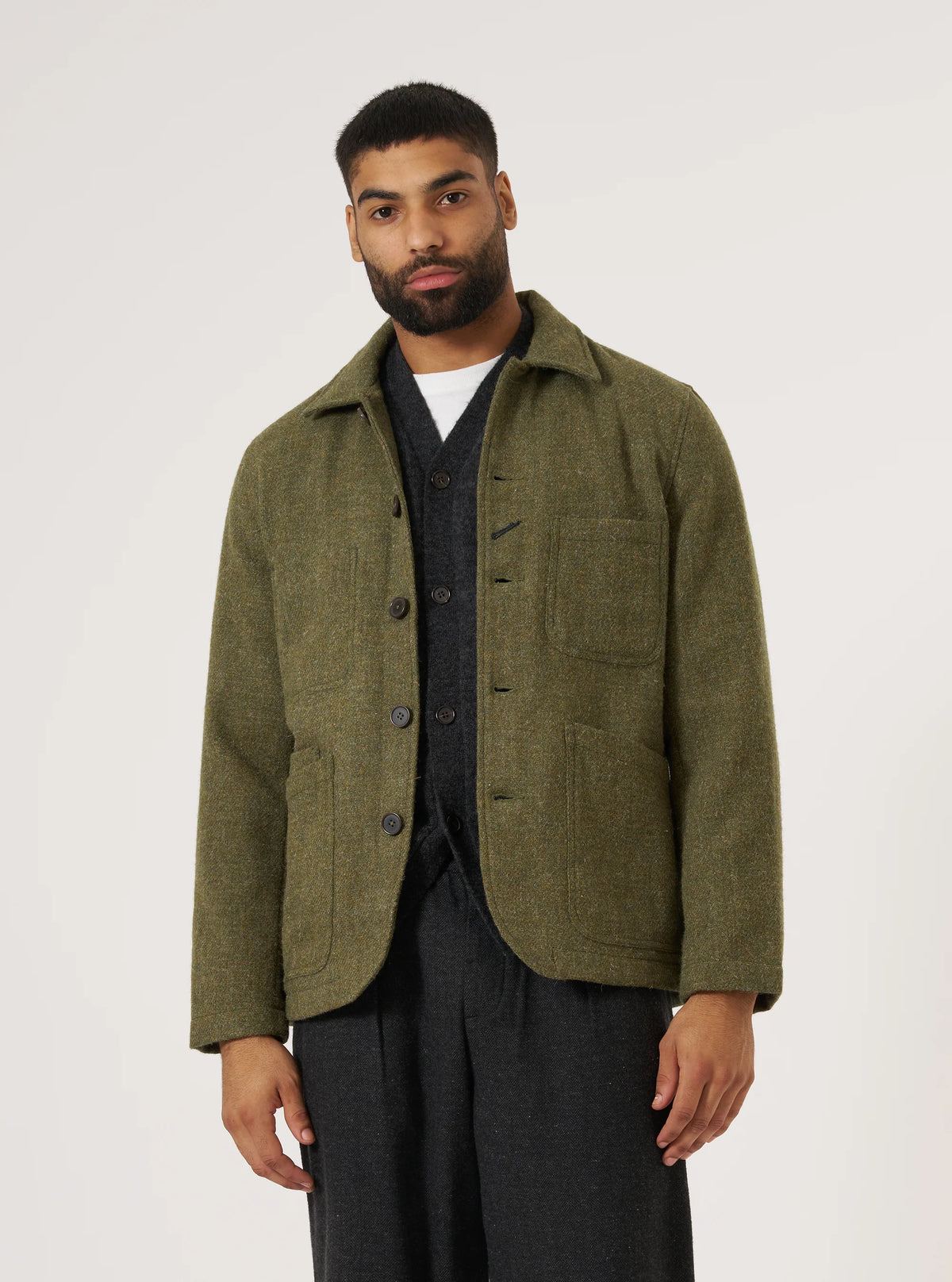 A model on a white background wears a Green Harris Tweed Plaid Bakers Jacket. The jacket is paired with a gray cardigan and dark pants.