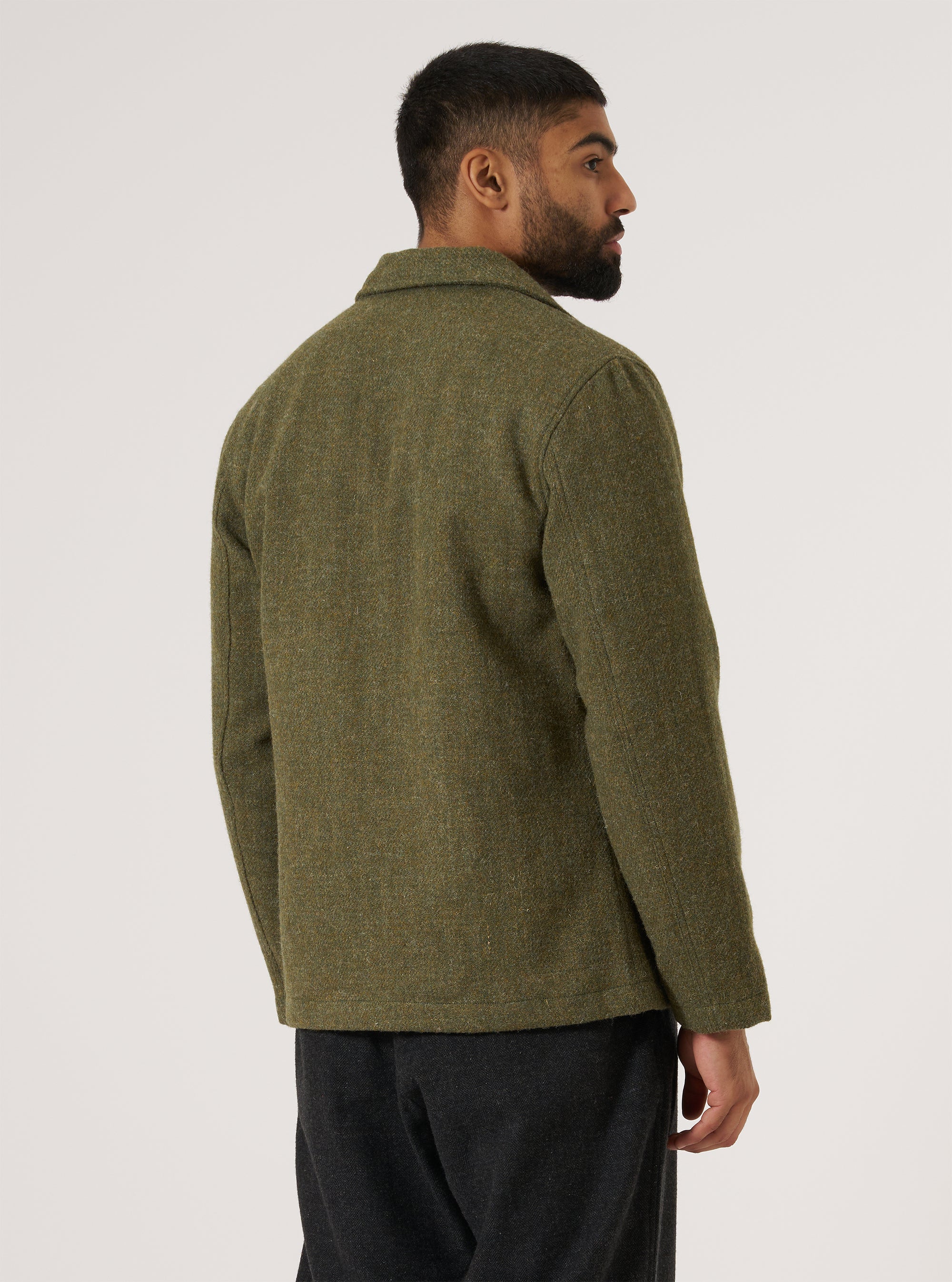 Profile of a model wearing a Green Harris Tweed Plaid Bakers Jacket. The jacket is green tweed. Shot against a white background.