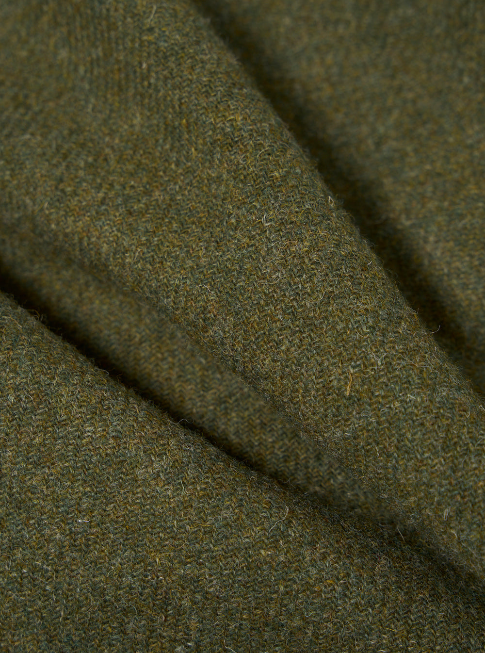 Close up of the green Harris Tweed Plaid Bakers Jacket fabric. The material is a textured wool in shades of green and brown. The image is tightly cropped.