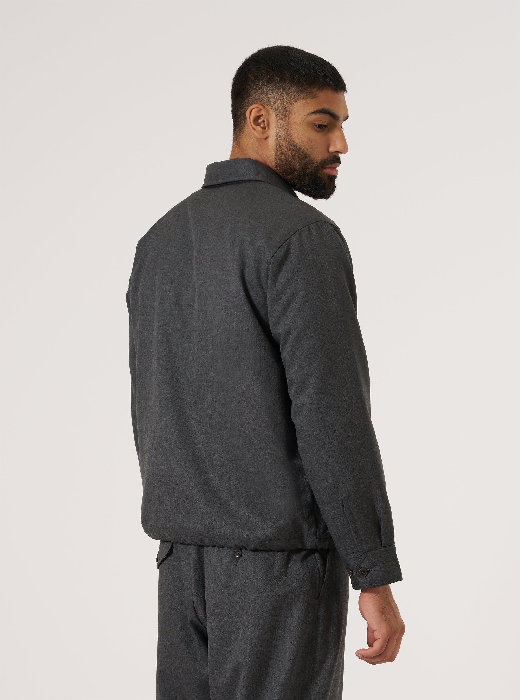 A man in a Charcoal Travel Suiting Padded Club Jacket and matching pants, shot from the back against a white background. The jacket has a relaxed fit and visible seams.
