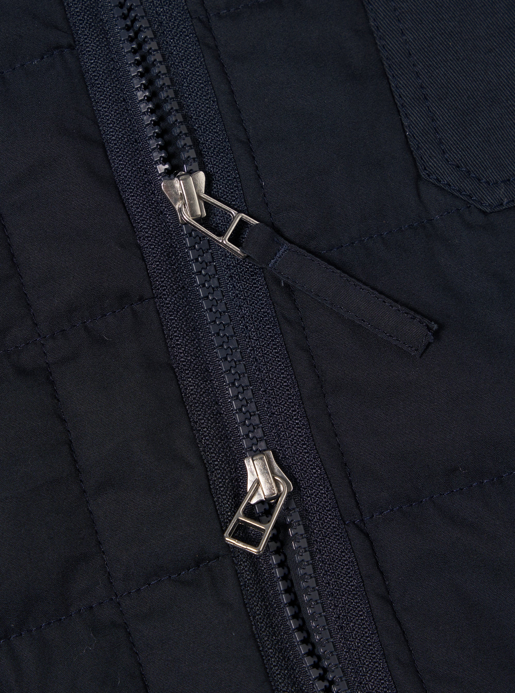 Close-up of the Navy Quilt Cotton Military Liner Jacket, showcasing the zipper detail and quilted cotton texture. The jacket is navy blue. 