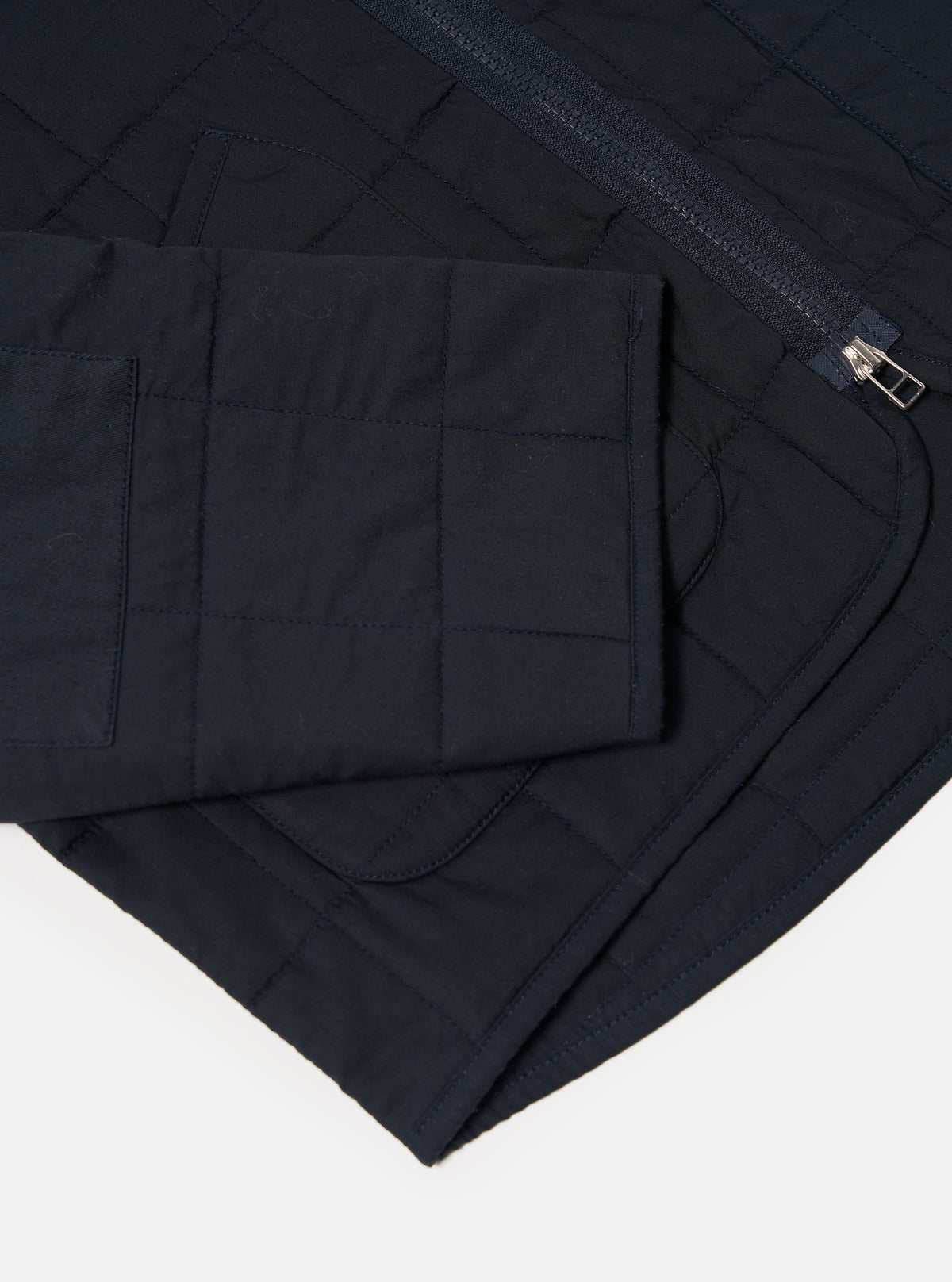 Close-up of the navy quilted cotton Military Liner Jacket on a white background, showcasing the material, stitching, zipper and pocket.