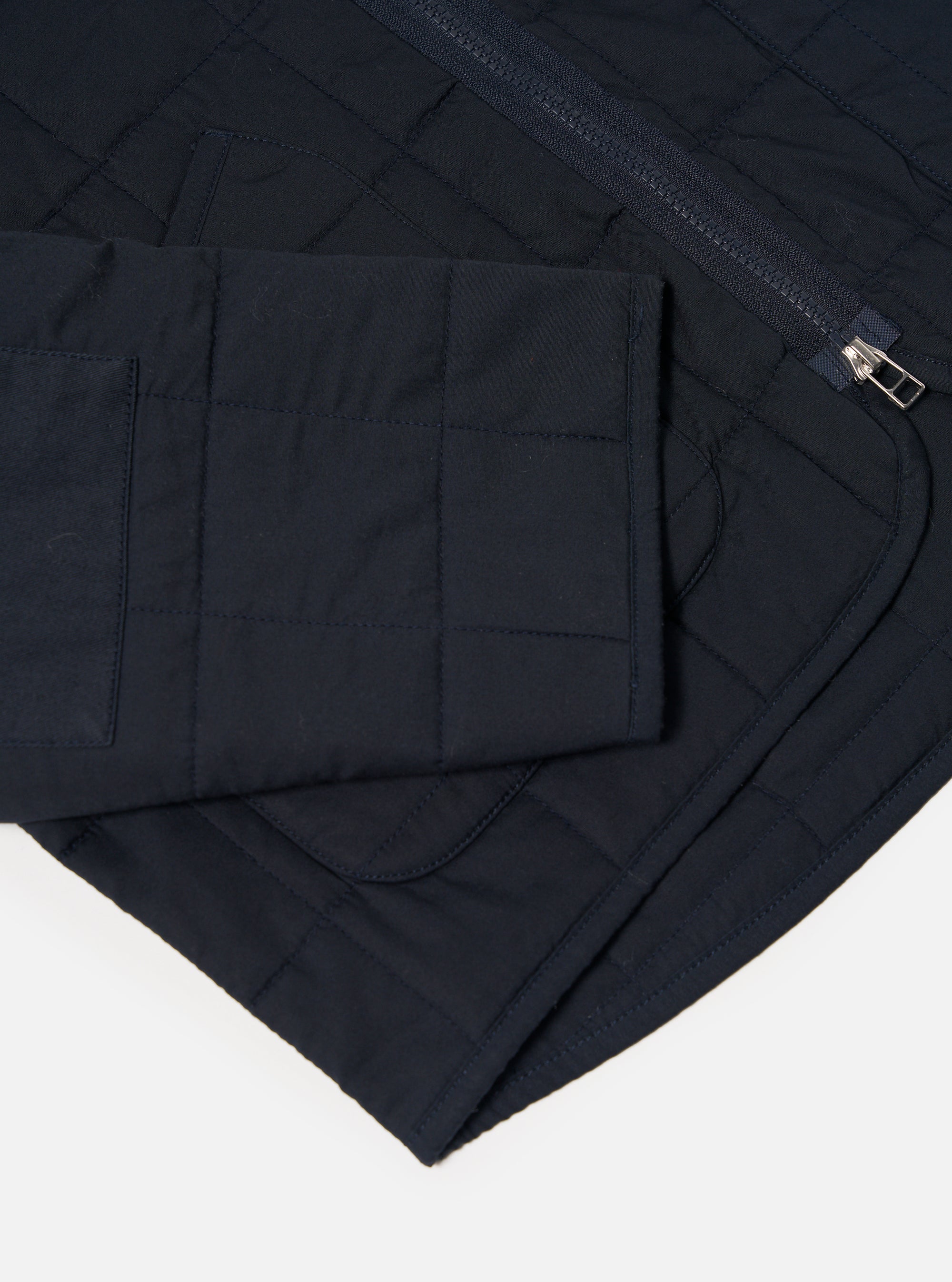 Close-up of the navy quilted cotton Military Liner Jacket on a white background, showcasing the material, stitching, zipper and pocket.