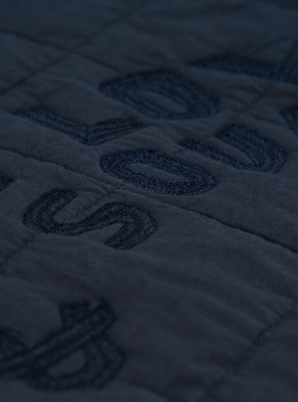 Close-up of the navy quilted cotton Military Liner Jacket, showing the texture and stitching detail on a flat surface. The jacket is a deep navy color.